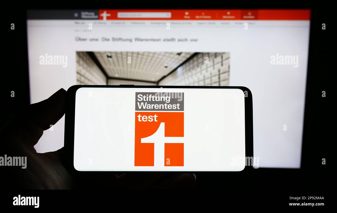 Personne tenant un smartphone avec le logo de l'organisation allemande des consommateurs Stiftung Warentest à l'écran devant le site Web. Mise au point sur l'affichage du téléphone. Banque D'Images