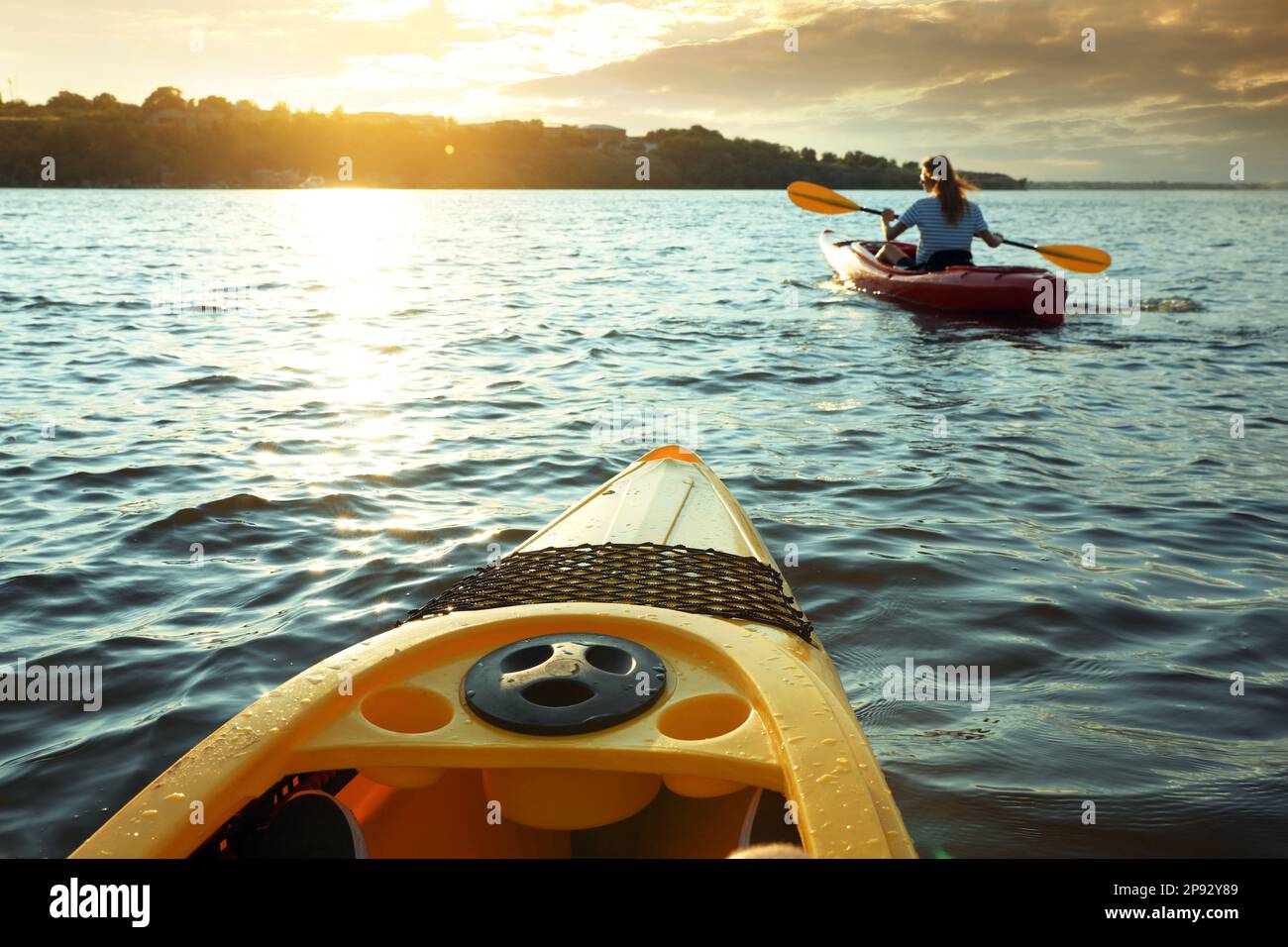 Femme kayak sur la rivière au coucher du soleil, vue depuis un autre bateau. En été Banque D'Images Femme kayak sur la rivière au coucher du soleil, vue depuis un autre bateau. En été Banque D'Images