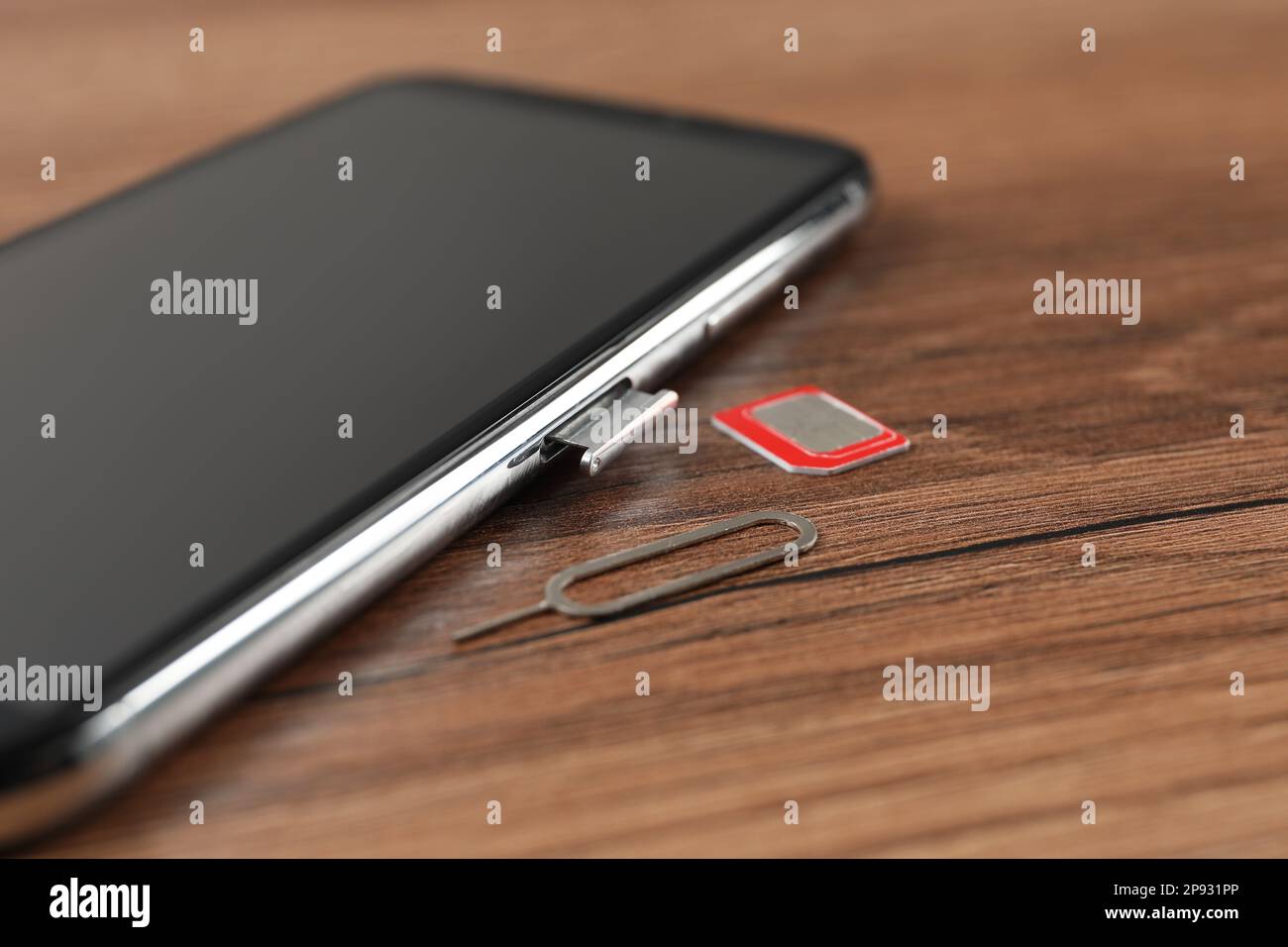 Téléphone mobile, carte SIM et outil d'éjection sur table en bois, gros plan Banque D'Images