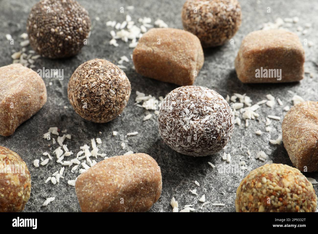 Différentes délicieuses boules de bonbons végétaliens et noix de coco déshydratée sur table grise Banque D'Images