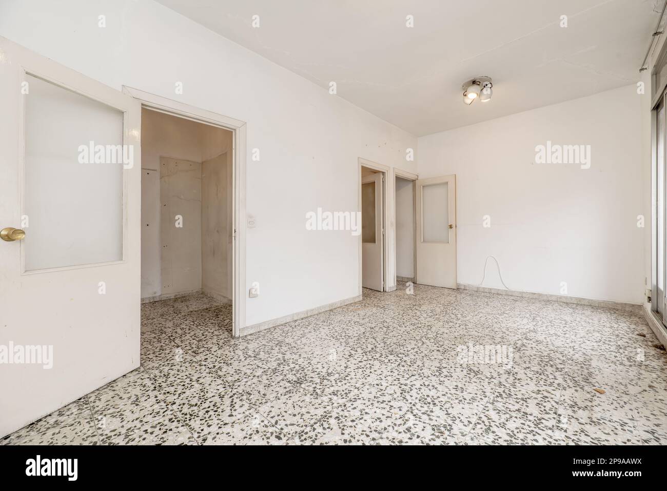 Cette chambre présente des murs peints en blanc, un sol en terrazzo avec des points noirs et des portes en bois blanc avec du verre Banque D'Images