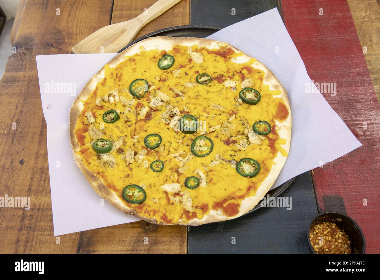 Une pizza à croûte mince fraîchement cuite avec du poulet, du fromage jaune, des tranches de jalapenos sur une plaque de cuisson recouverte de papier parchemin Banque D'Images