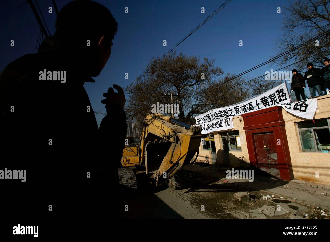 A Chinese resident smokes outside his house, during a protest against a forceful eviction at his home, set to be demolished, in Beijing, China, Saturday, Dec. 20, 2008. The banners read "Forceful demolition. Seven lives, who cares? So much corruption" and "No Human rights, depriving us from our life. Forcing a happy family to the path of death". The area is set to be demolished to make way for new real estate developments. (AP Photo/ Elizabeth Dalziel) Banque D'Images
