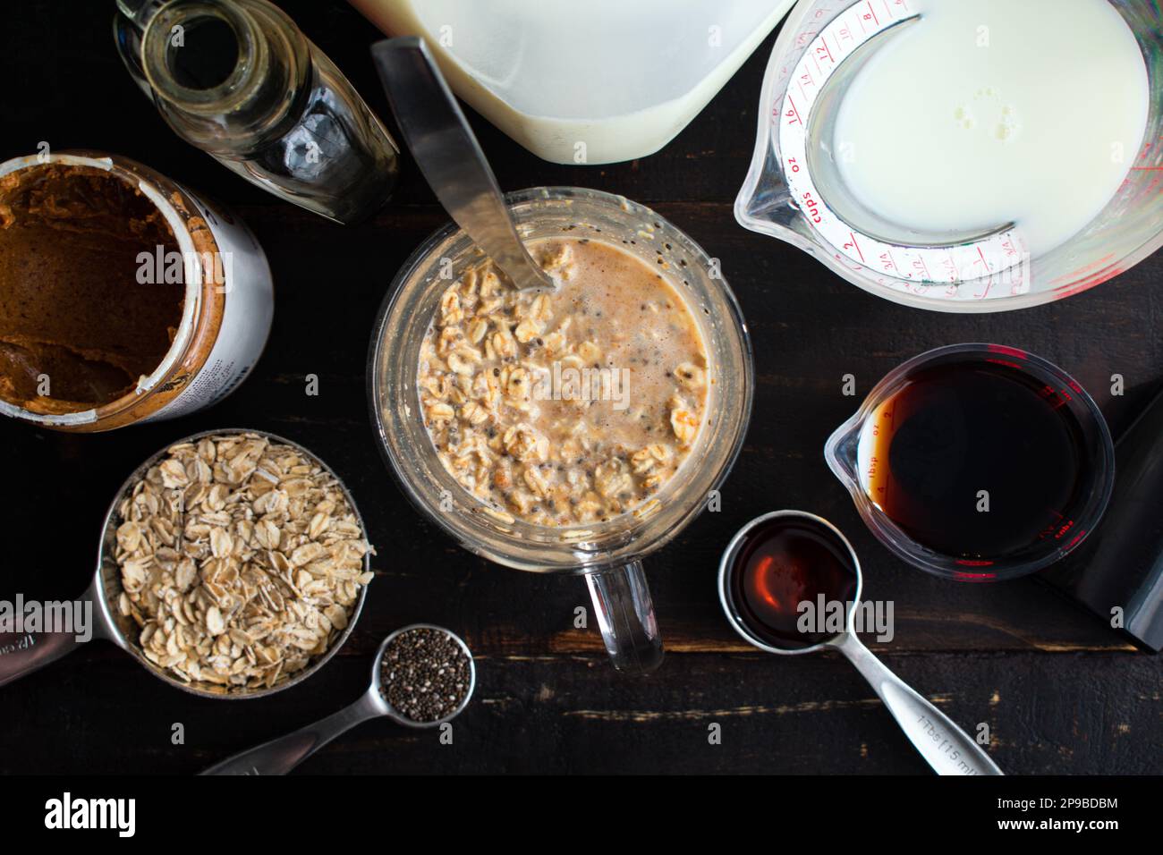 Mélange d'ingrédients pour la préparation froide à la vanille Oats de nuit dans un mug en verre : faire des flocons d'avoine de nuit dans un mug en verre entouré des ingrédients Banque D'Images
