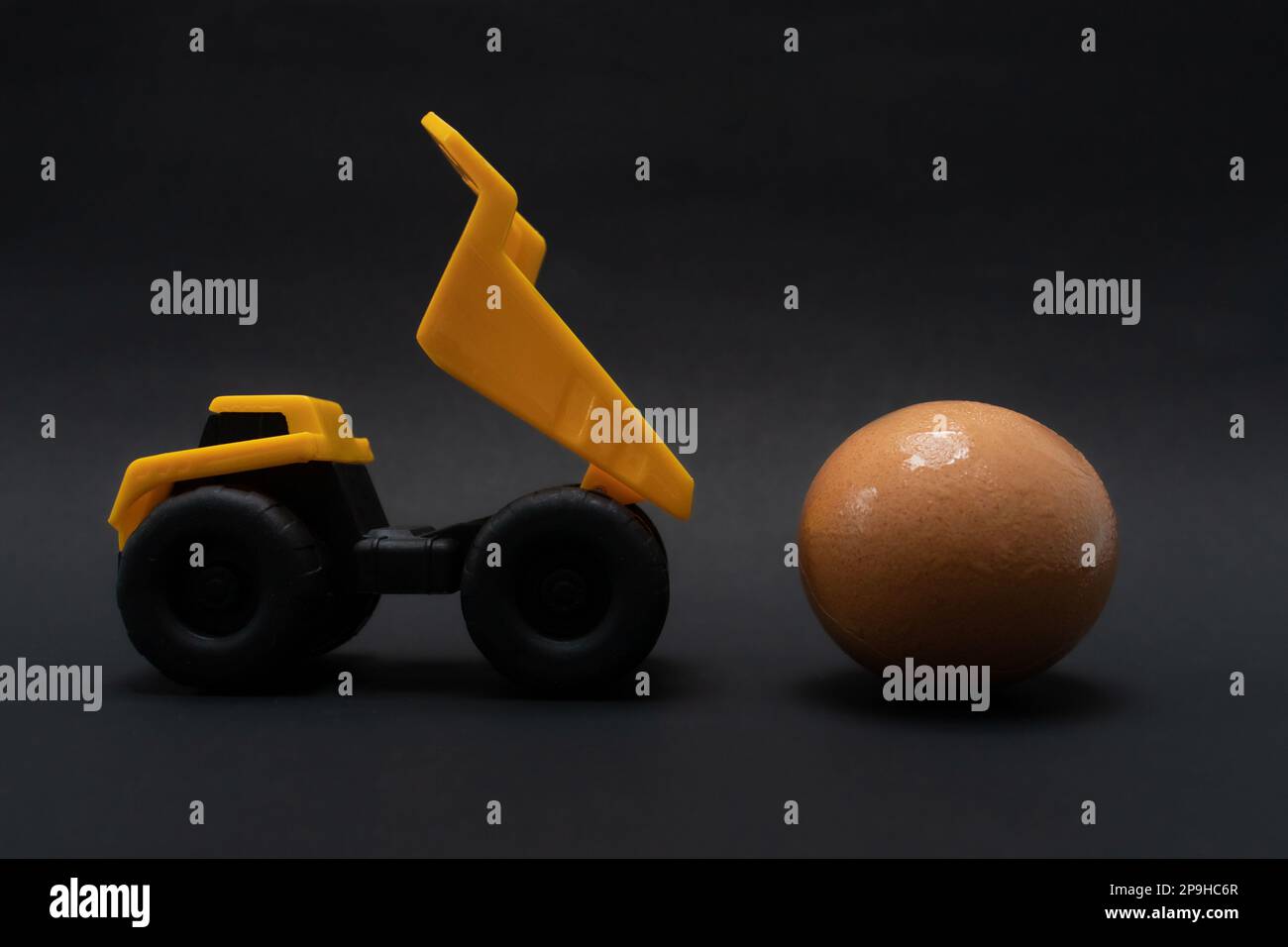 Une photo après quelques modifications, un camion jaune tente de transporter un œuf, sur papier de fond noir. Banque D'Images