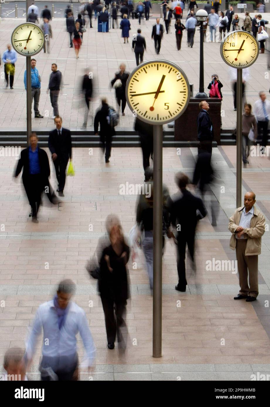 People walk past clocks in the Canary Wharf business district of London, Monday, Oct. 13, 2008. The British government injected an unprecedented 37 billion pounds (US$63 billion) into the country's leading banks Monday to avoid a full-scale collapse of the sector. In return for the rescue, the Royal Bank of Scotland Group PLC, Lloyds TSB Group PLC and HBOS PLC will cede major stakes to the government and halt cash bonuses for bank board members this year. (AP Photo/Matt Dunham) Banque D'Images