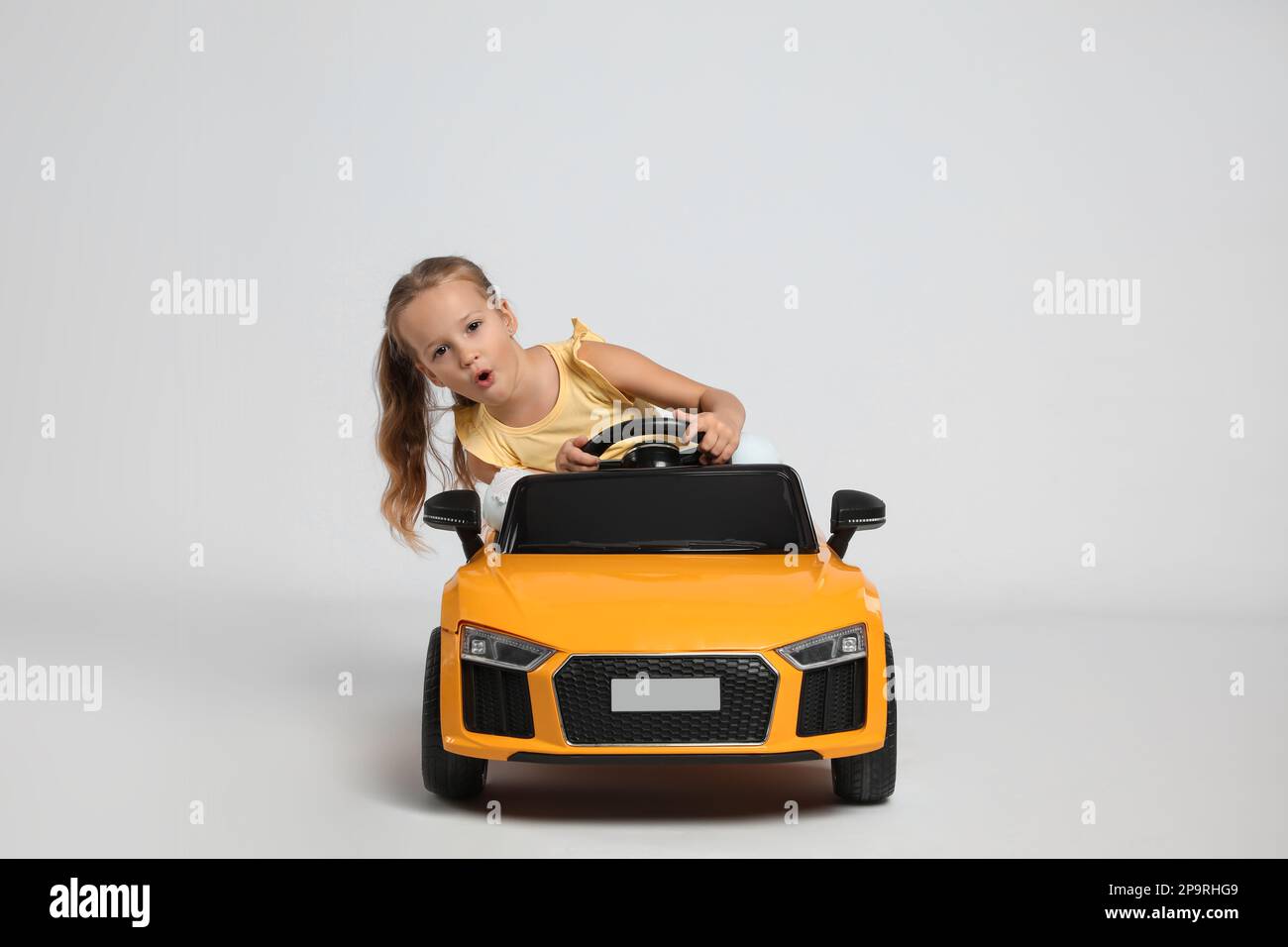 Jolie petite fille conduisant la voiture électrique des enfants sur fond  gris Photo Stock - Alamy