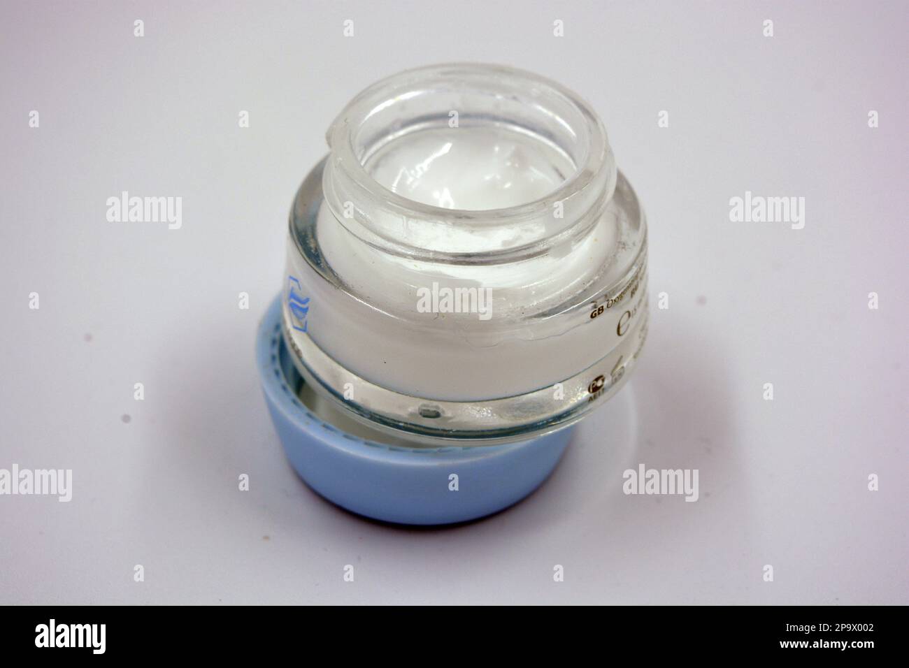 Agréable, parfumé, crème blanche pour le visage, soin du visage dans une épaisse bouteille de verre, un pot avec un couvercle bleu et est situé sur un fond blanc. Banque D'Images