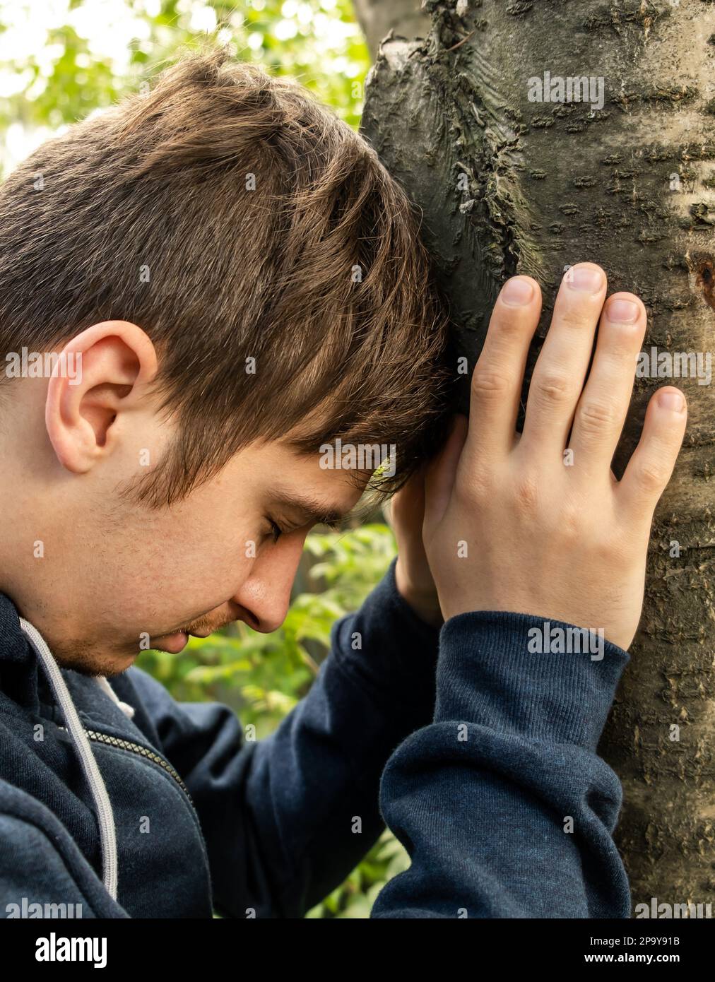 Jeune homme touche un tronc de l'arbre à l'extérieur Banque D'Images