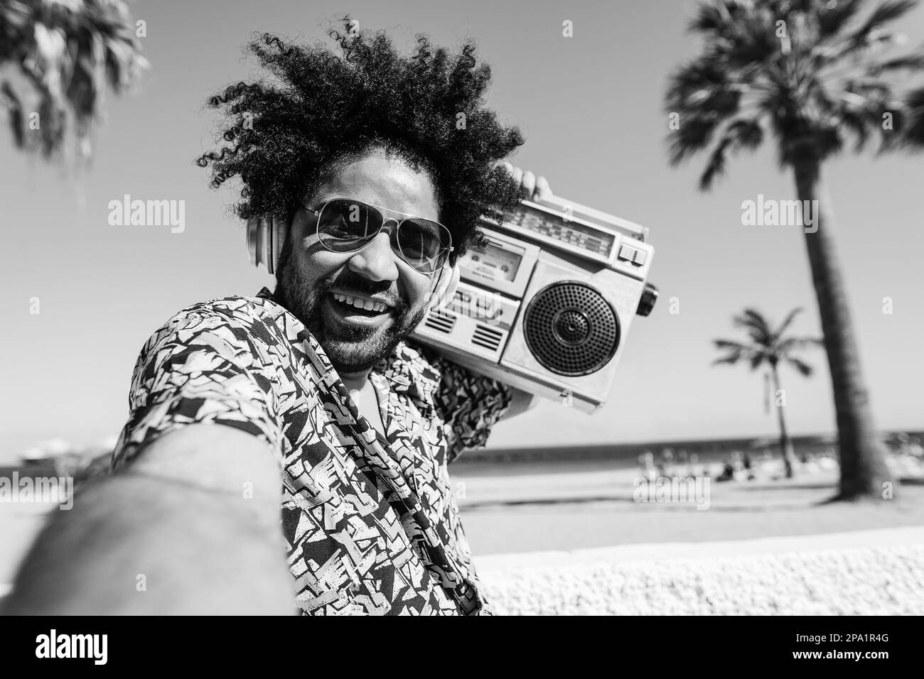 Homme africain écoutant de la musique avec boombox stéréo vintage extérieur avec plage en arrière-plan - Focus sur le visage - montage noir et blanc Banque D'Images