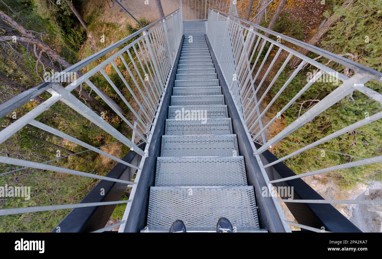 Escaliers métalliques menant à la forêt depuis une plate-forme d'observation avec des pieds mâles en chaussures bleues au premier plan dans le Surselva près de Flims en Suisse Banque D'Images