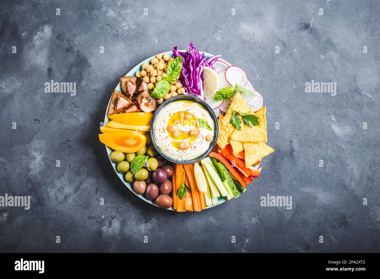 Plateau de houmous avec assortiment d'en-cas. Houmous dans un bol, bâtonnets de légumes, pois chiches, olives, chips de pita. Plaque avec méze de l'EasternMediterranean du milieu. Banque D'Images