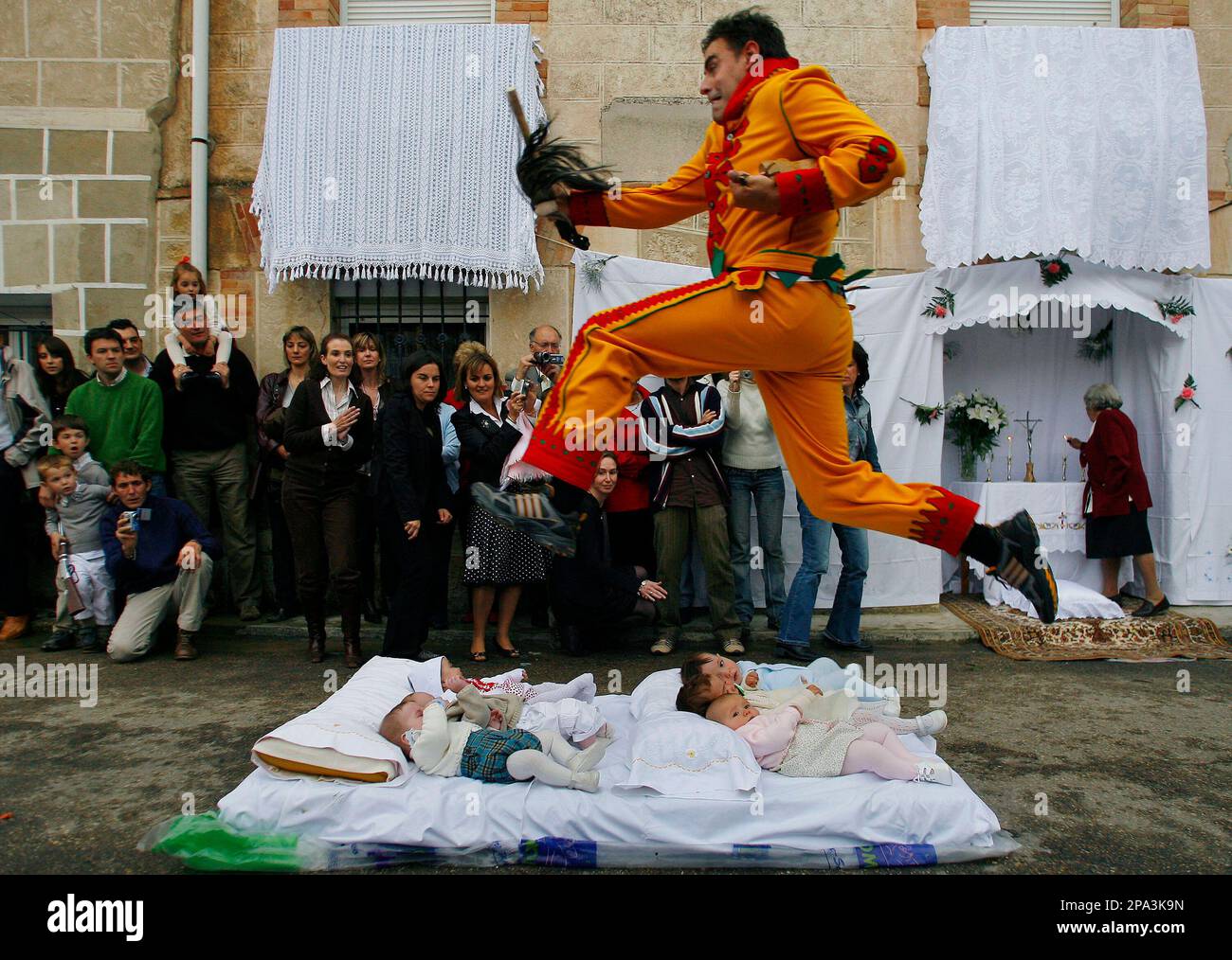 A man representing the devil and dressed in a traditional red and yellow costume, known as El Colacho, jumps over babies placed on a mattress in Castrillo de Murcia, Spain, Sunday, May 25, 2008. 'El Colacho' has been jumping over babies during the traditional celebration of Corpus Christi for centuries in an unusual ritual to protect them from evil spirits. (AP Photos/ Israel L.Murillo) Banque D'Images