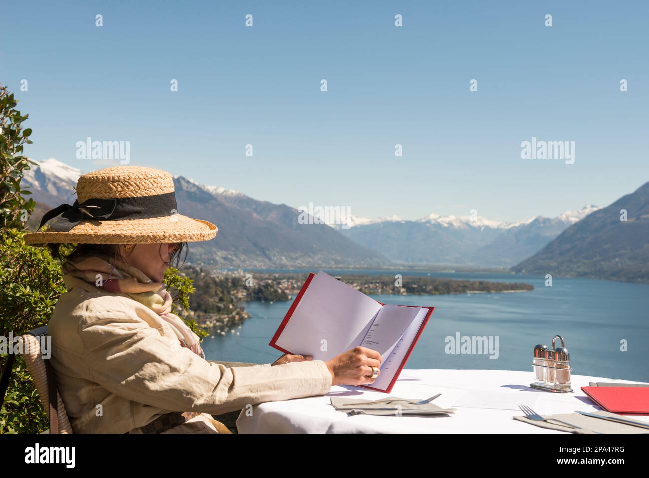 Femme avec chapeau de paille assis et lisant le menu dans un restaurant  avec vue panoramique sur le lac majeur en une journée ensoleillée à Ascona,  Tessin, Suisse Photo Stock - Alamy