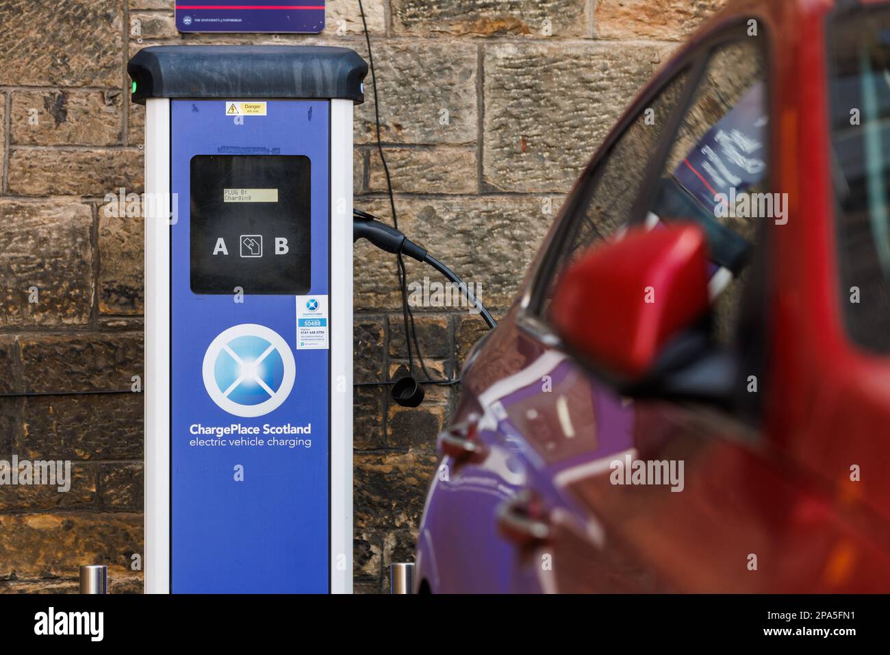 Un véhicule électrique rouge est branché à une unité de charge électrique de ChargePlace Scotland sur le campus de l'Université d'Édimbourg. Banque D'Images