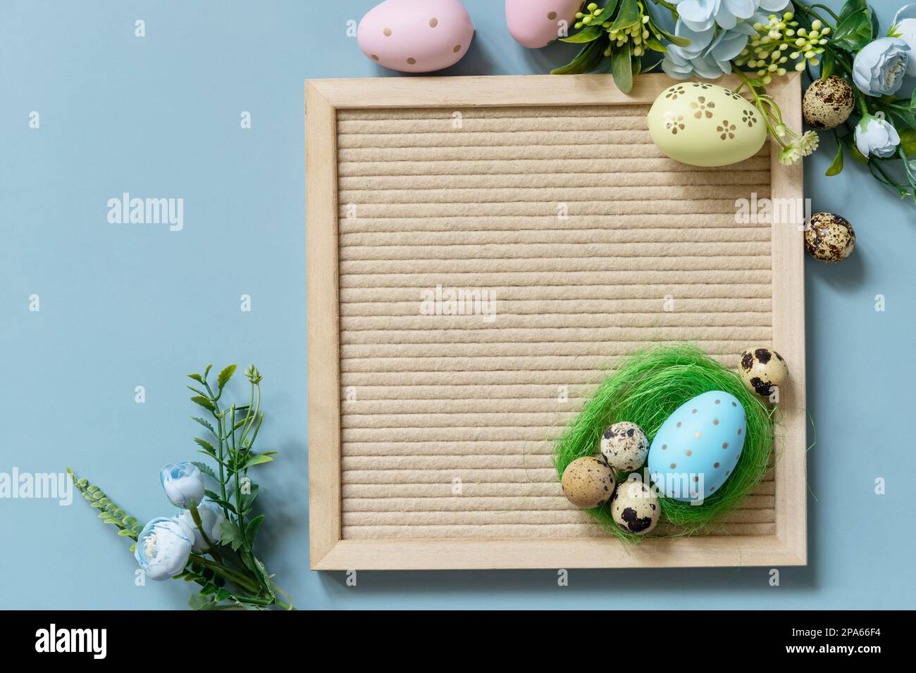 Concept d'accueil printanier. Tableau de lettres, œufs de Pâques et fleurs de printemps sur fond bleu pastel, composition de style minimaliste. Vue de dessus. C Banque D'Images