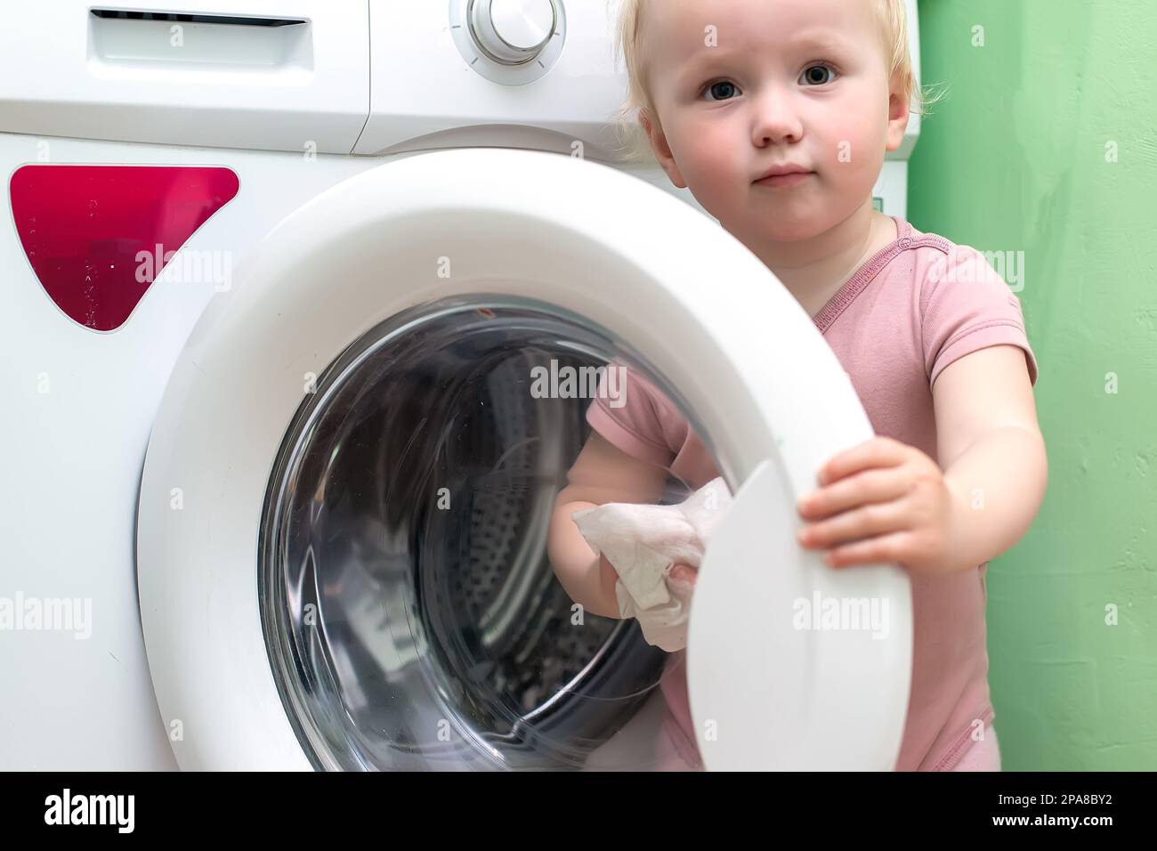 nettoyage pour tout-petits laver la machine à laver. la petite fille nettoie la porte ouverte d'un lave-linge blanc à la maison avec un chiffon humide. Maintenir la propreté de Banque D'Images