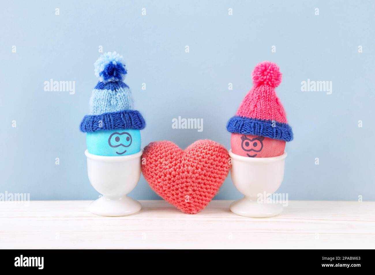 Deux œufs de Pâques aux visages amusants et chapeaux crochetés dans des supports blancs et un coeur crocheté sur une table en bois. Concept joyeuses Pâques. Carte de vœux. Banque D'Images