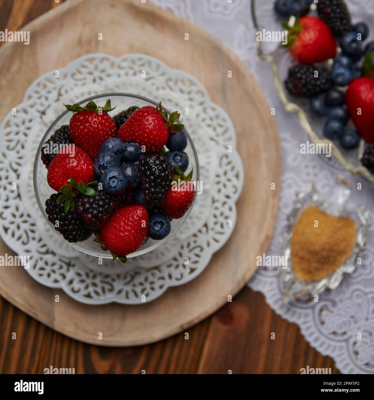Dessert aux baies sur table avec assiette blanche et chargeur de bois. Fraises, baies noires et baies bleues. Banque D'Images