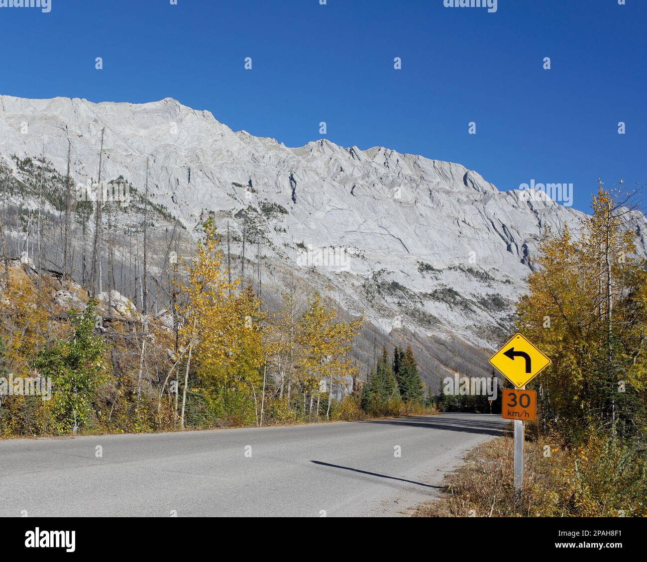 Signalisation routière avec limite de vitesse de 30 km/h et avertissement pour la courbe à venir sur une route à travers les montagnes avec ciel bleu dans le parc national Jasper, Canada Banque D'Images