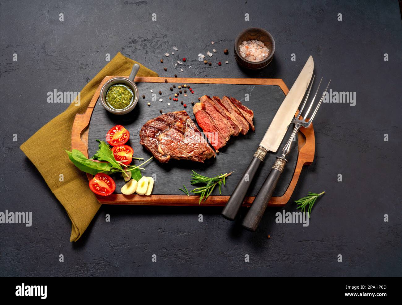 Steak de bœuf à la ribeye grillé, sauce chimichurri, herbes et épices sur une table sombre. Steak en tranches sur le tableau noir pour le steak Banque D'Images