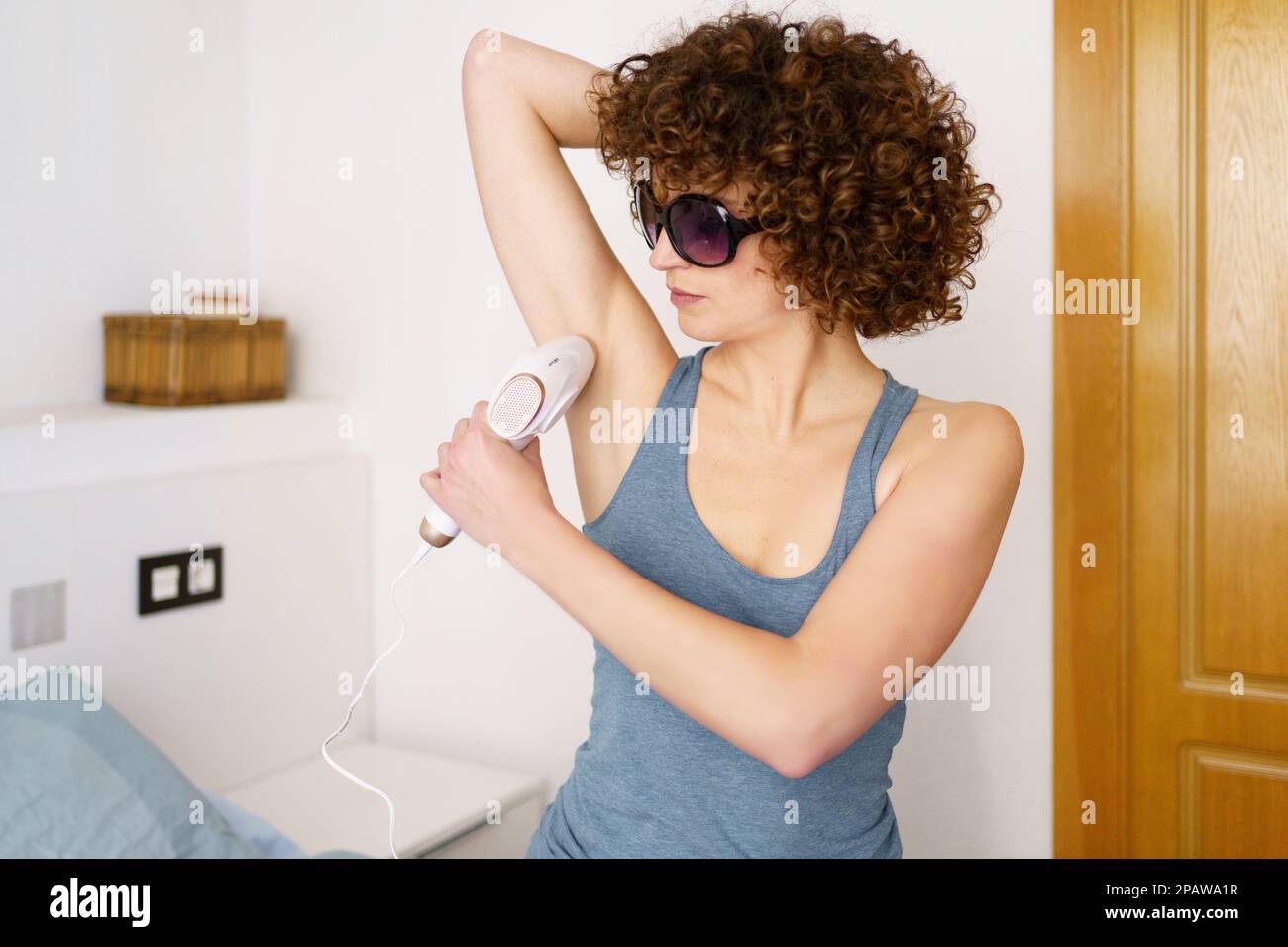 Femme concentrée qui retire les poils des aisselles avec la lumière intense pulsée à l'aide de lunettes de protection Banque D'Images