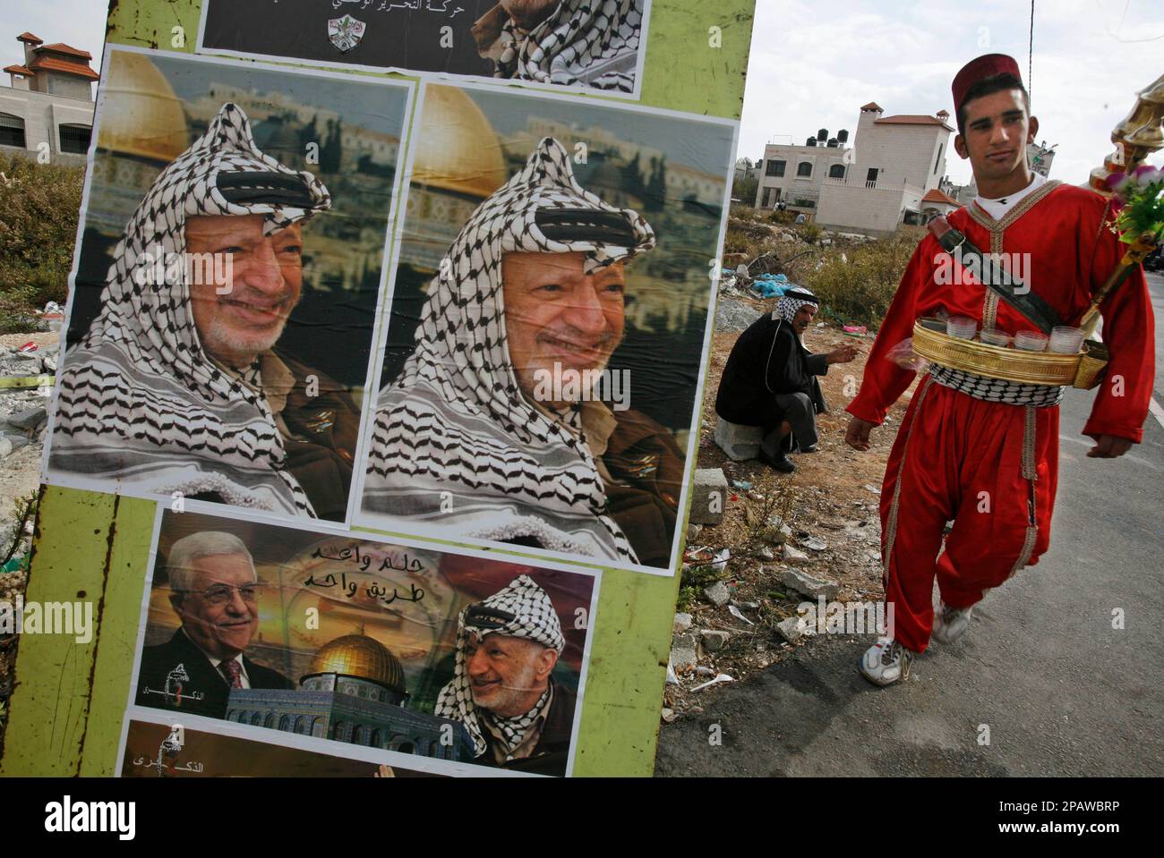 A Palestinian juice vendor walks past posters of the late leader Yasser Arafat outside a ceremony to mark the third anniversary of Arafat's death and the opening to the public of his new grave at President Mahmoud Abbas' headquarters in the West Bank town of Ramallah, Sunday, Nov. 11, 2007. Arafat died Nov. 11, 2004 after leading the Palestinians for nearly four decades. (AP Photo/Kevin Frayer) Banque D'Images
