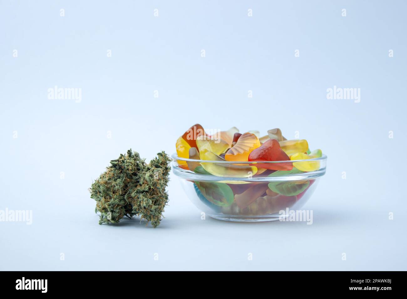 Des gummies assorties dans un petit bol en verre à côté de plusieurs bourgeons de marijuana médicale. Sur fond bleu pâle, beaucoup d'espace vide Banque D'Images