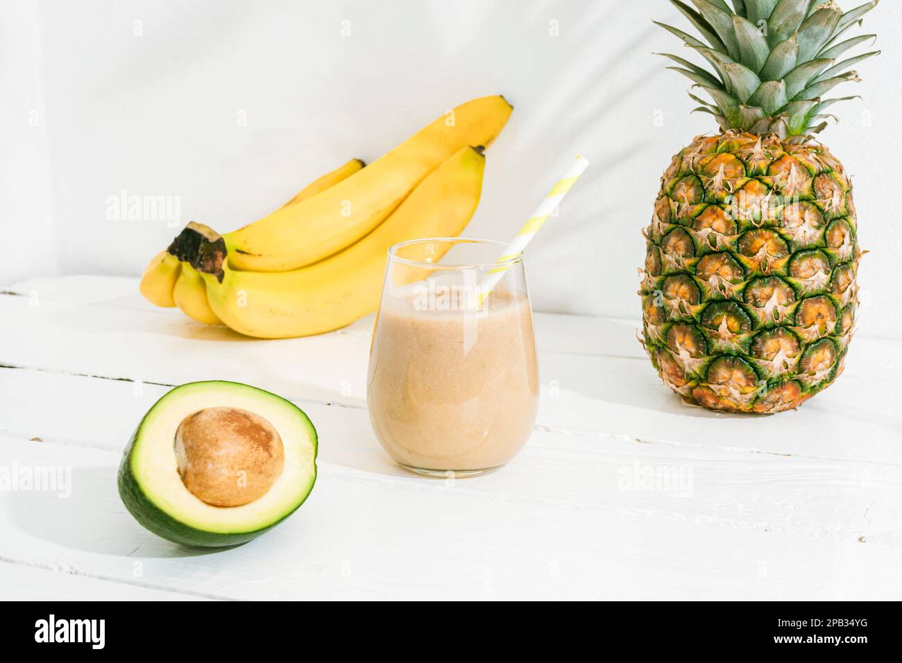 Smoothie à la banane, à l'ananas et à l'avocat sur une table en bois blanc au soleil. Concept minimal de diète de détox, boisson de vitamine d'été. Banque D'Images