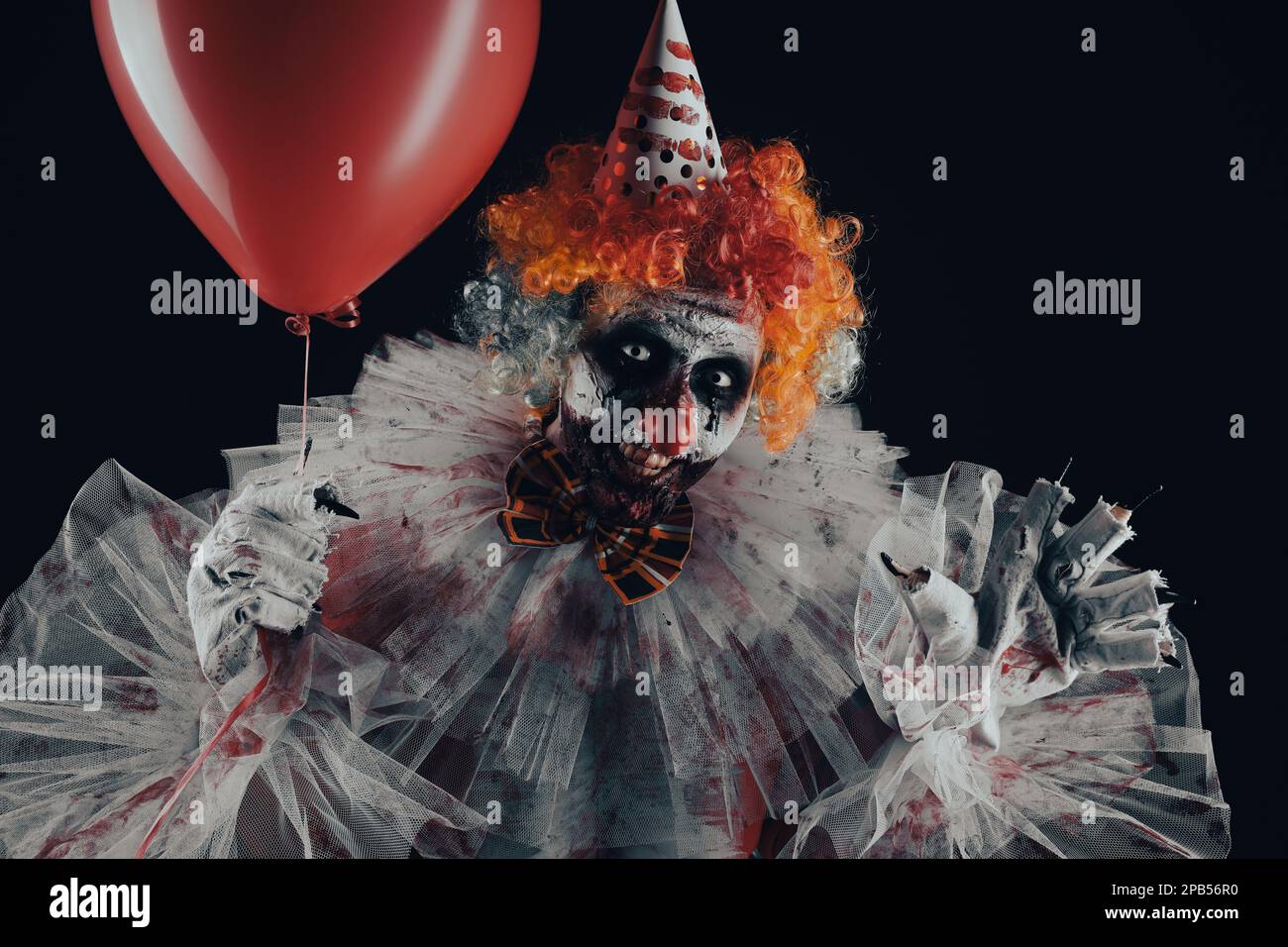 Clown terrifiant avec ballon d'air rouge sur fond noir. Costume de fête d'Halloween Banque D'Images