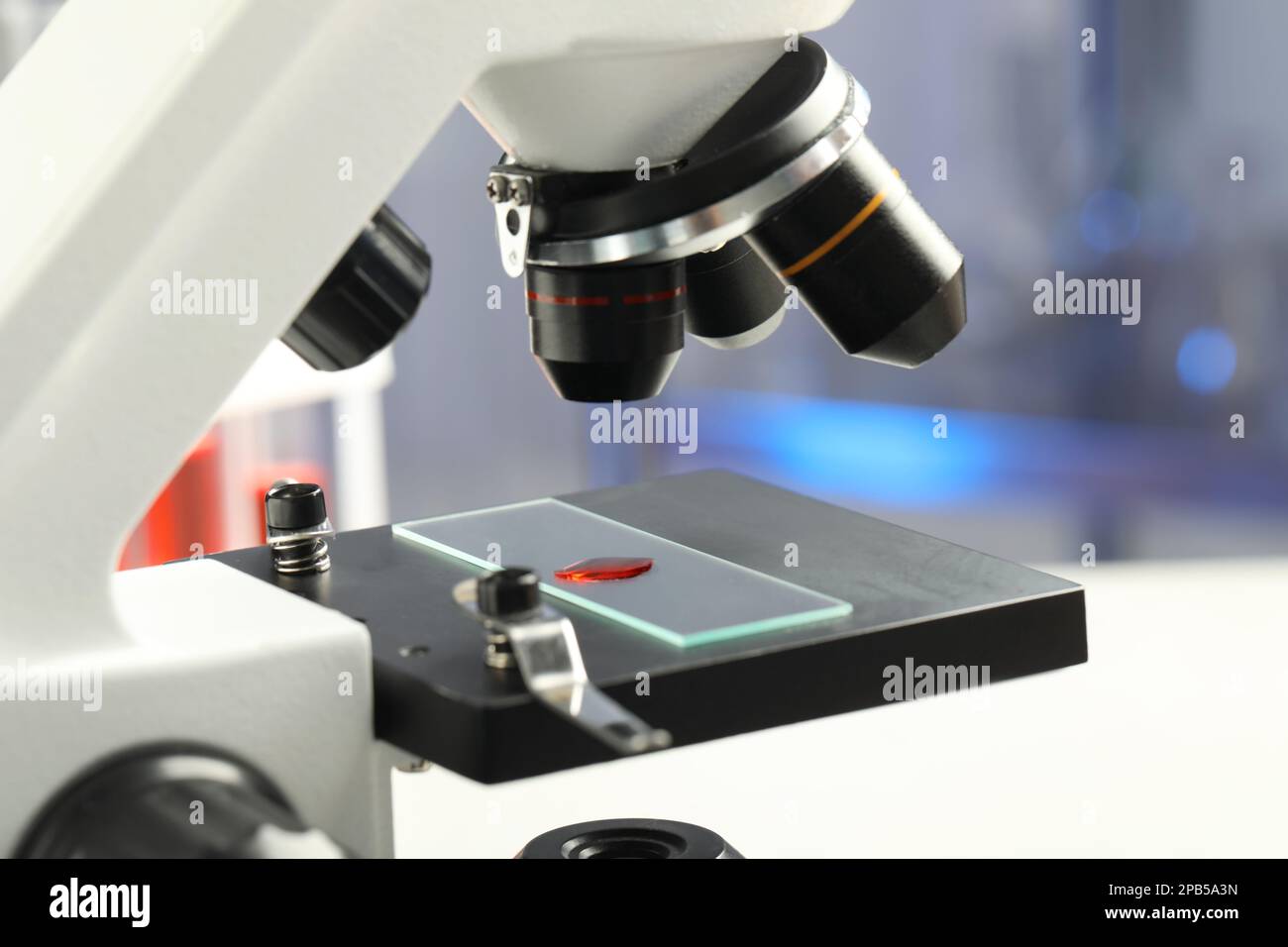Lame de verre avec échantillon de liquide rouge sous microscope en laboratoire, gros plan Banque D'Images