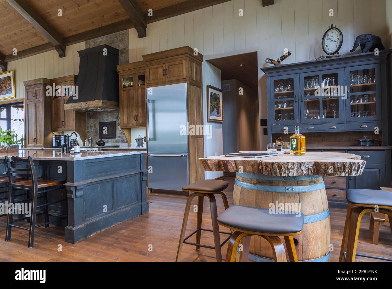 Ancienne île en bois de pin au charbon de bois avec comptoir en granit gris  clair nuancé et armoires en bois de cerisier coloré, bar à baril de whisky  avec tabourets de