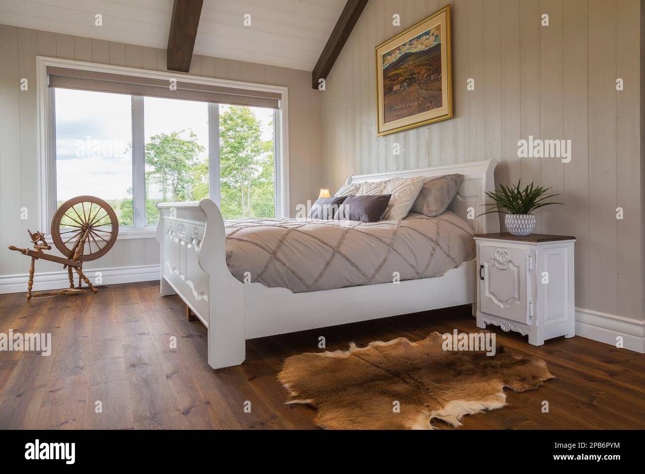 Grand lit double en traîneau peint en blanc dans la chambre principale avec des murs en bois brossé et des planchers en pin rouge à l'intérieur de la maison hybride en bois. Banque D'Images