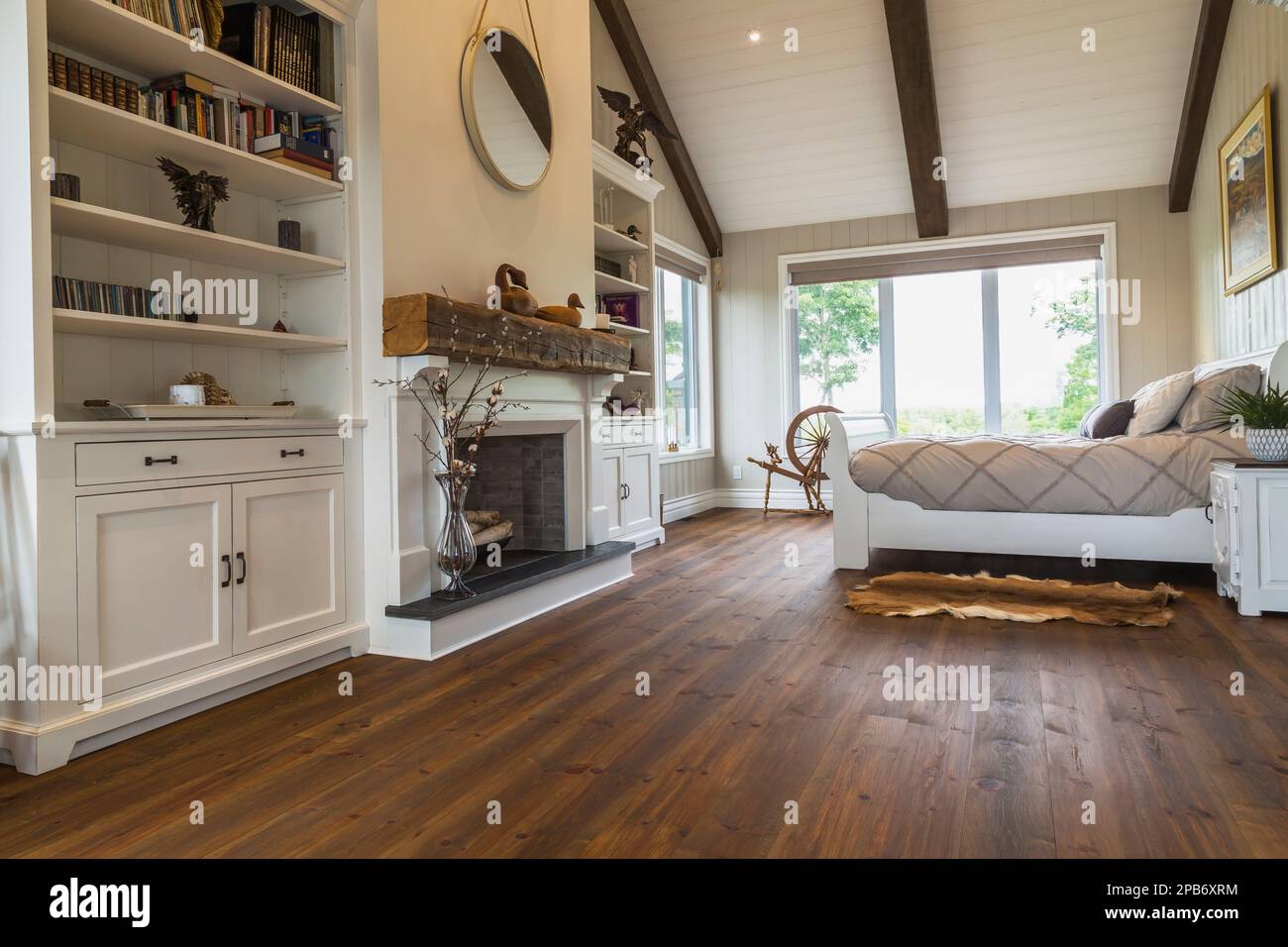 Grand lit double en traîneau peint en blanc dans la chambre principale avec cheminée décorative, murs en bois brossé, parquet en pin rouge à l'intérieur de la maison en bois. Banque D'Images