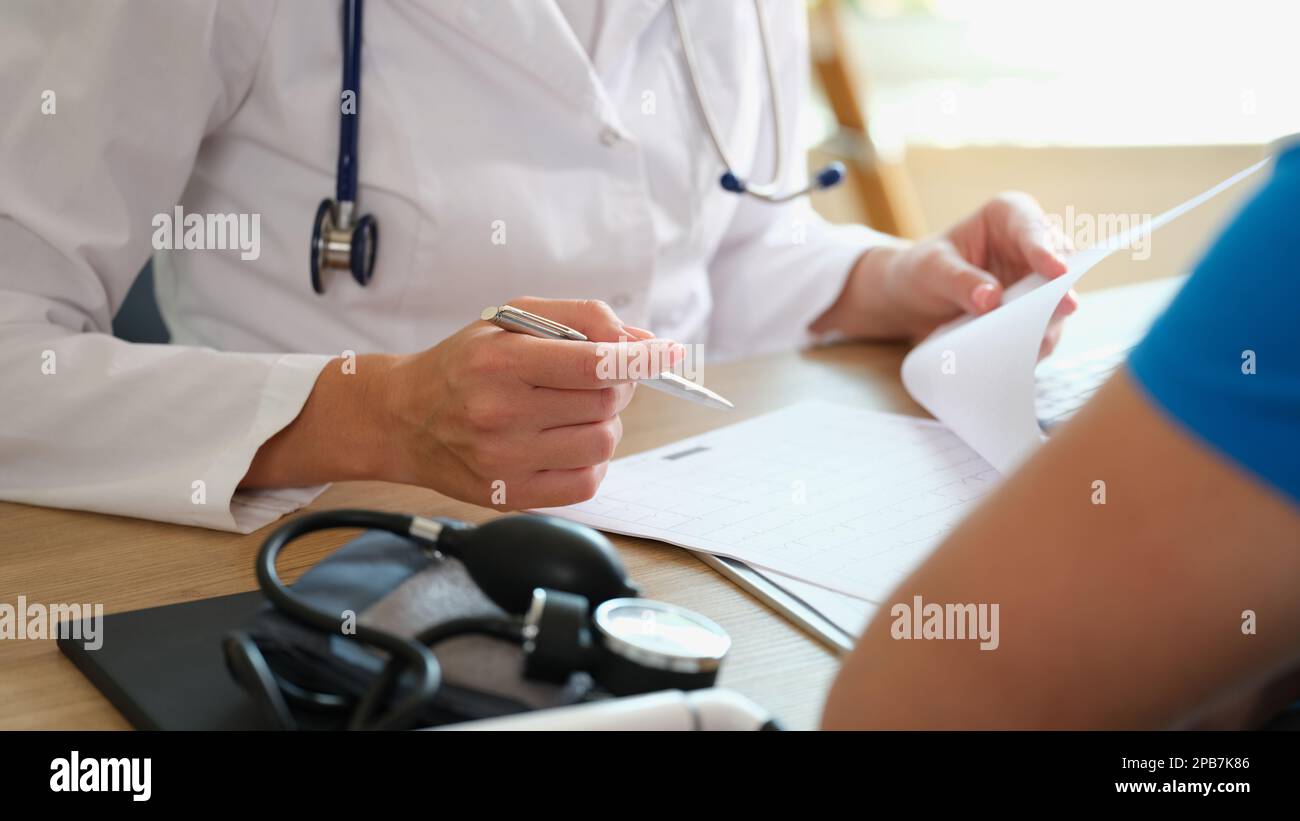 Le médecin prend des notes dans le document, assis à la table avec le patient. Banque D'Images