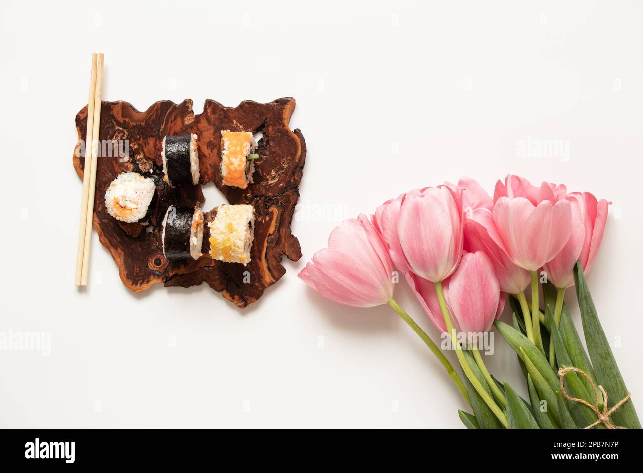 Le sushi se trouve sur une planche en bois à côté d'un bouquet de tulipes roses sur fond blanc, un dîner de vacances Banque D'Images