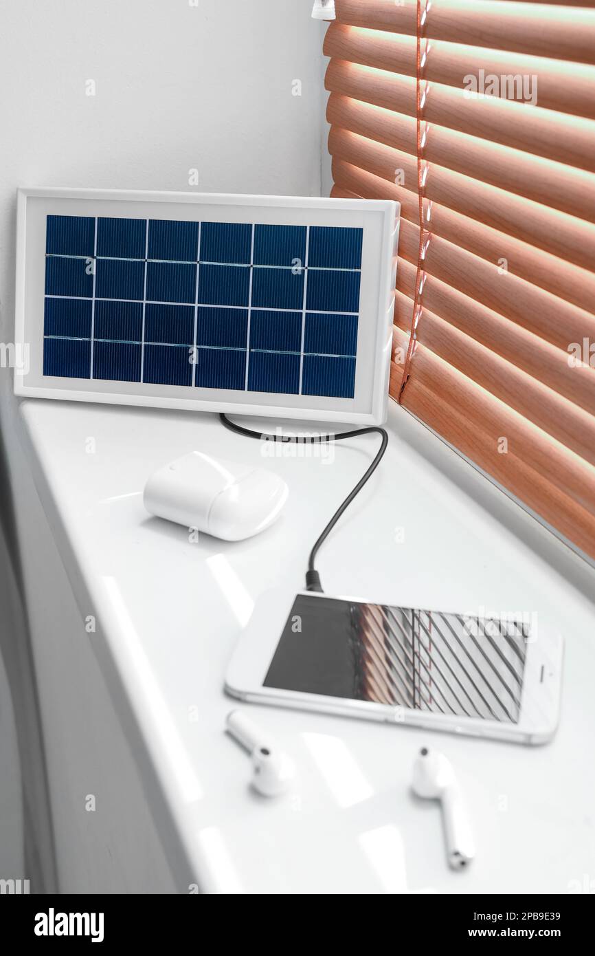 Panneau solaire portable pour charger le téléphone portable et les écouteurs sur le rebord de la fenêtre dans la chambre Banque D'Images
