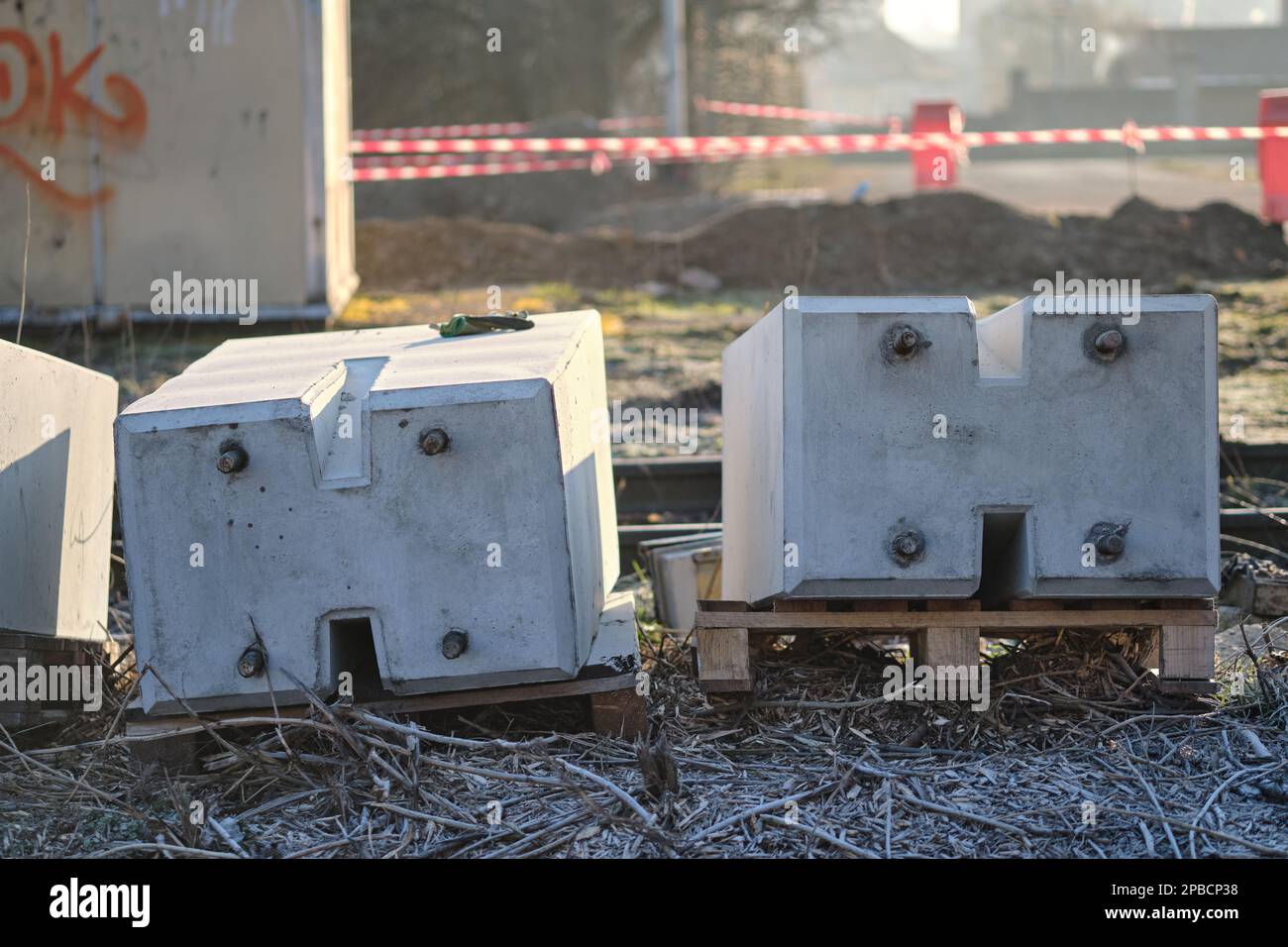 Blocs de béton sur des palettes préparés pour la construction d'un passage à niveau placé sur le sol avec l'infrastructure ferroviaire en arrière-plan Banque D'Images