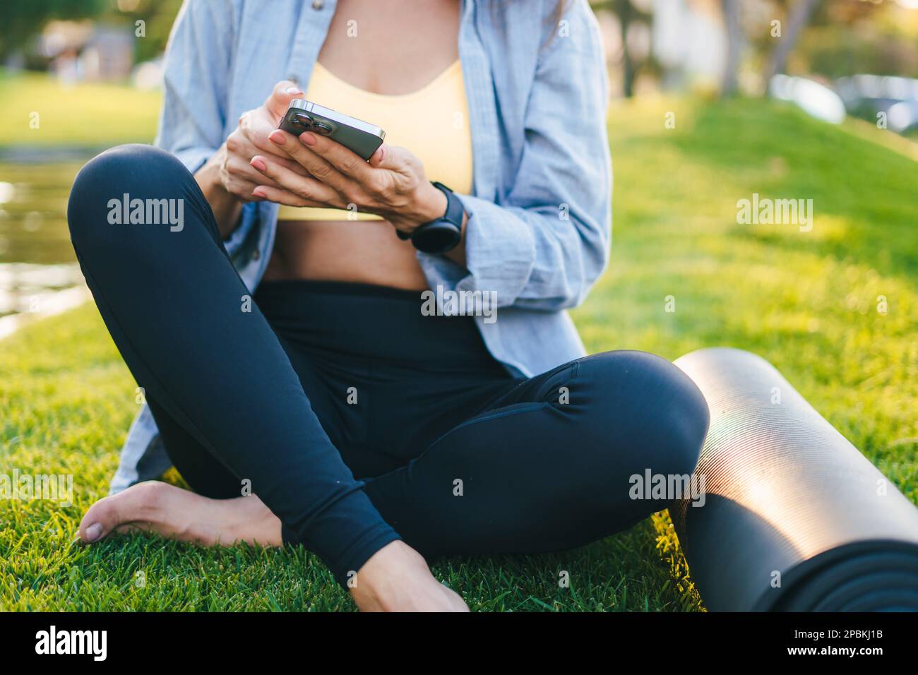 Femme sportive avec un téléphone portable dans la main, assis dans l'arrière-cour sur l'herbe verte, se reposant après les entraînements du matin. Femme de fitness. Vue en gros plan Banque D'Images