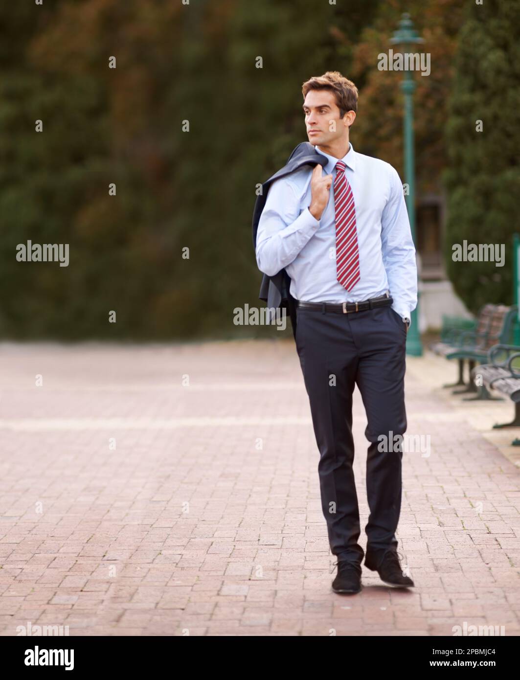 Promenade après le travail dans le parc. Un bel homme d'affaires marchant dehors avec sa veste sur son épaule. Banque D'Images