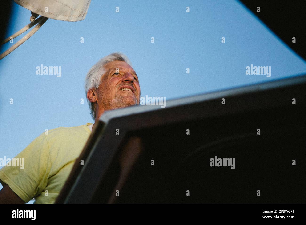 L'homme voile son bateau avec le vent dans ses cheveux gris avec le ciel bleu Banque D'Images