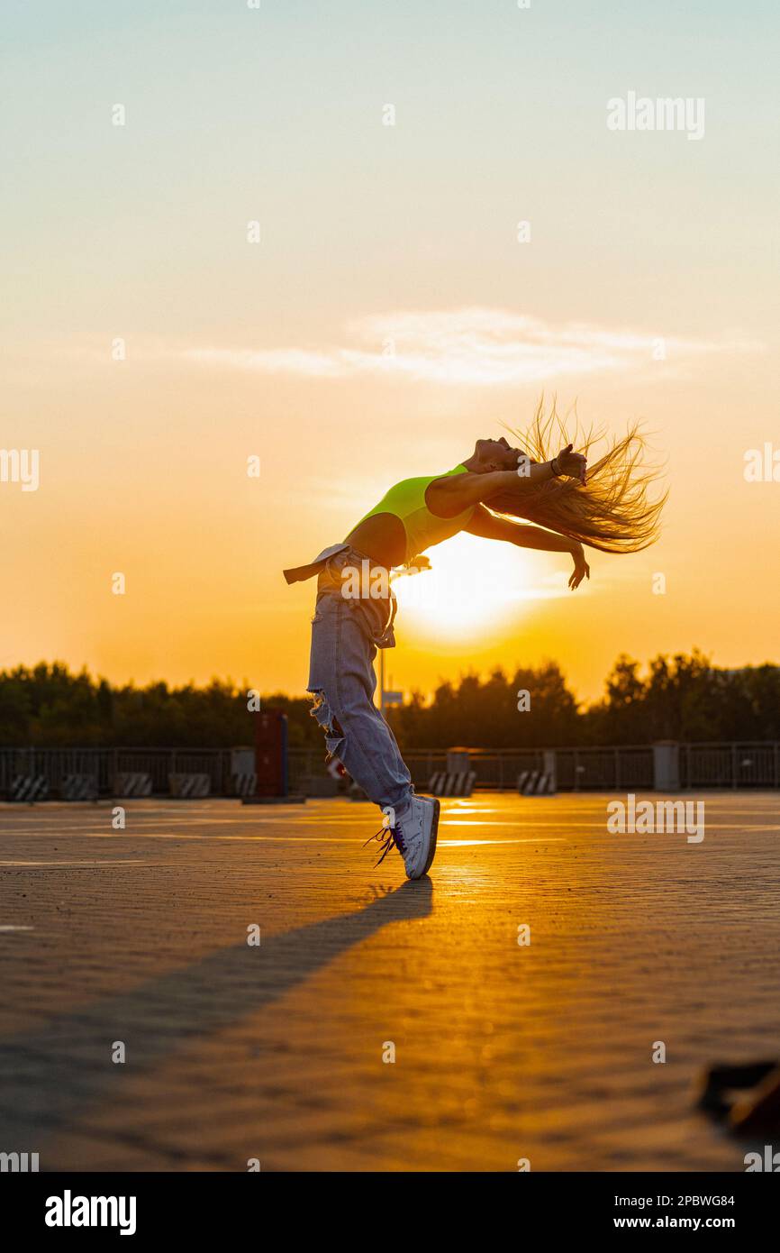 La femme danse au coucher du soleil, en mouvement, cheveux volants. Banque D'Images