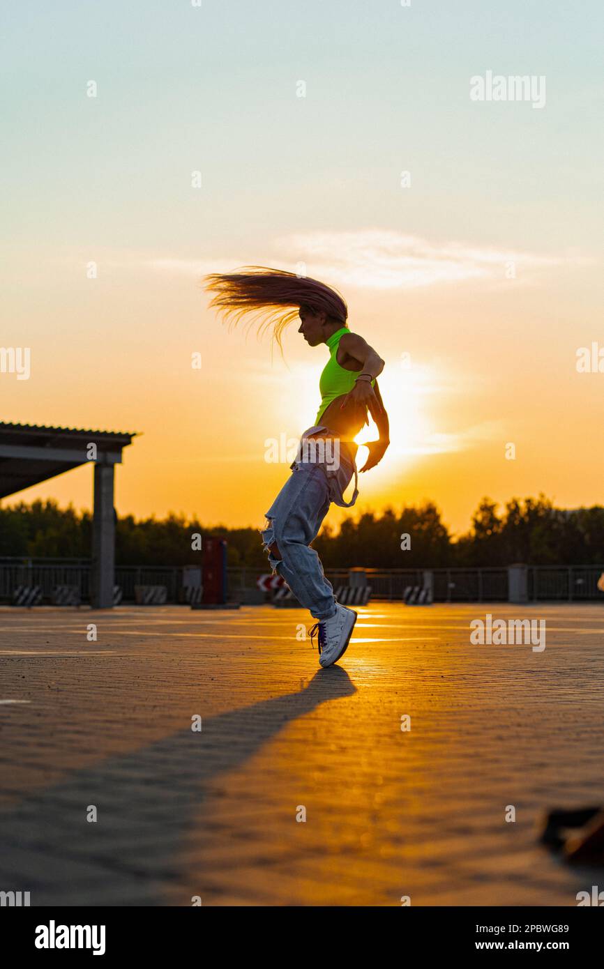 La femme danse au coucher du soleil, en mouvement, cheveux volants. Banque D'Images