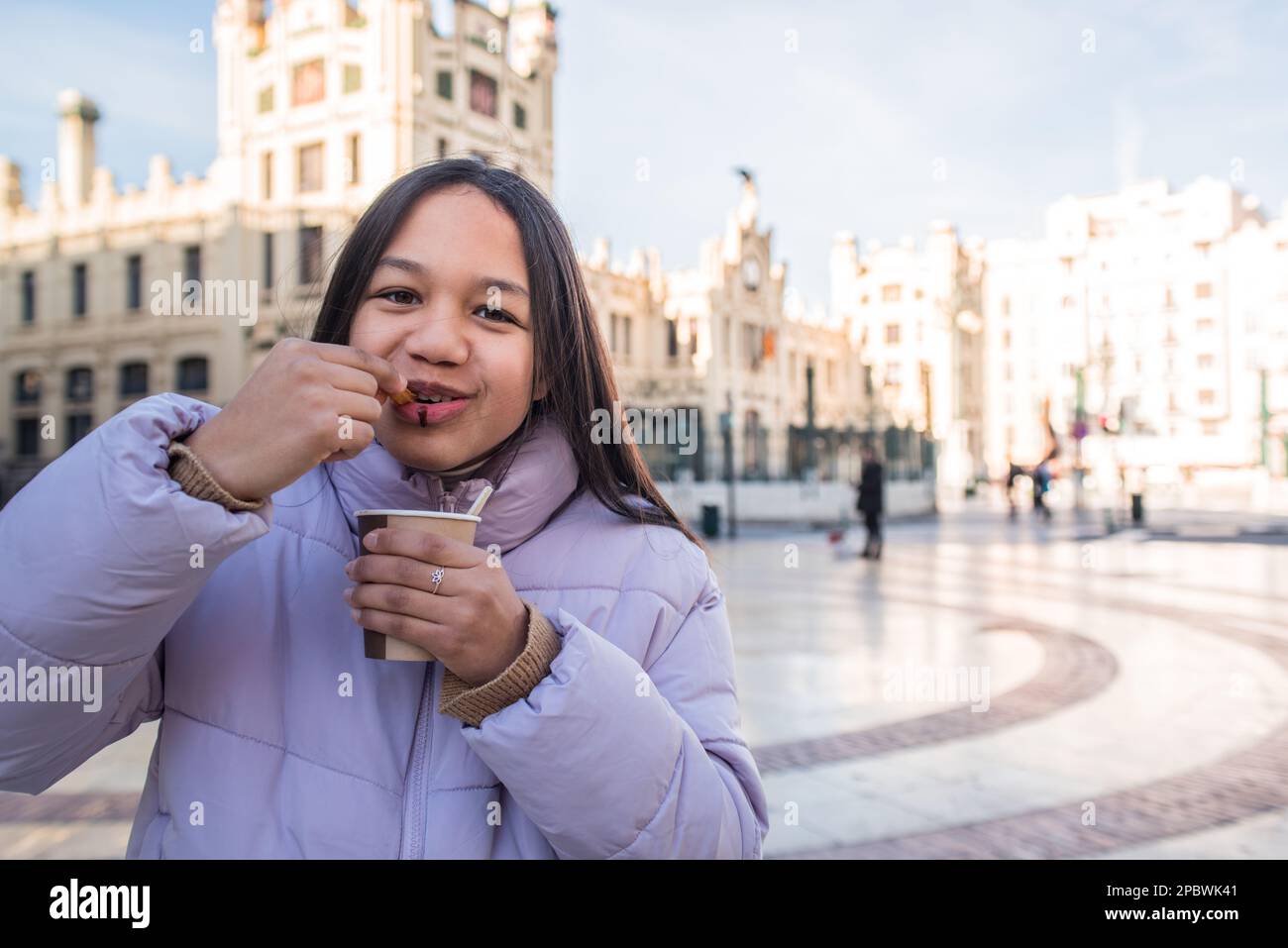 Une fille mangeant des churros tient une tasse de chocolat et regardant l'appareil photo. Banque D'Images