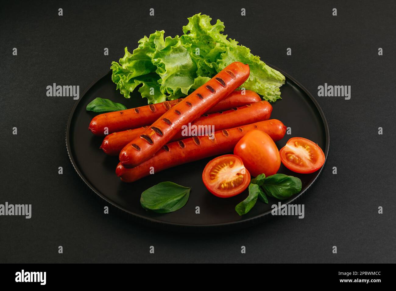 Saucisses grillées sur une assiette noire. Légumes et sauce. Banque D'Images