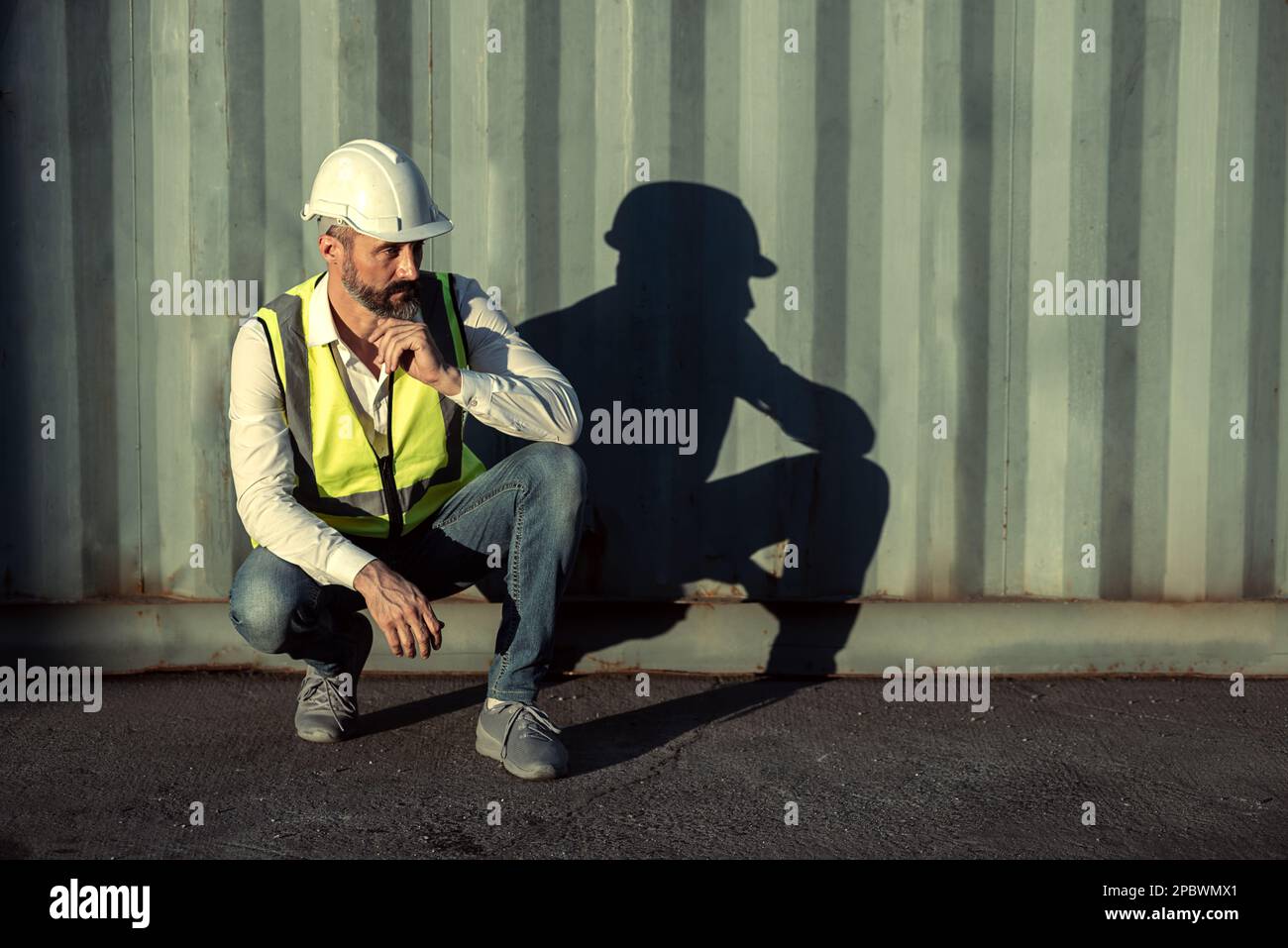Un ingénieur ou un travailleur assis près d'un conteneur de cargaison semble fatigué et sérieux après le travail dans la zone de travail. Banque D'Images