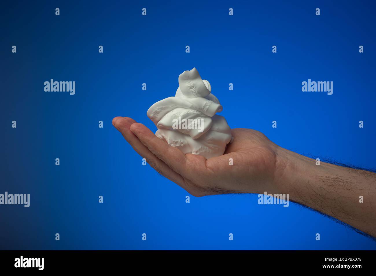 Mousse de rasage blanche maintenue dans la paume par un homme caucasien. Gros plan en studio, isolé sur fond bleu. Banque D'Images