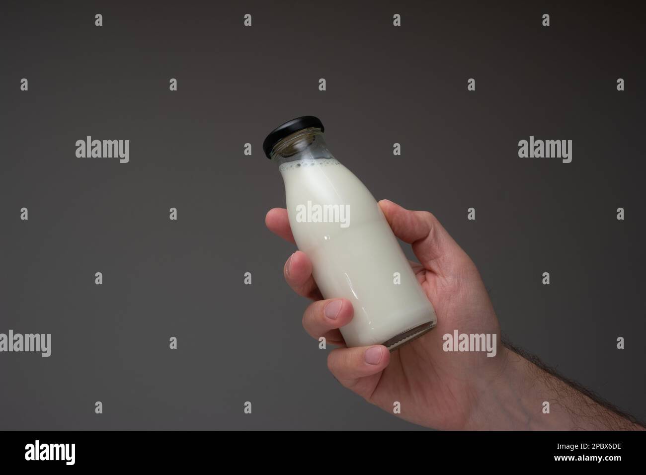 Petite bouteille de lait en verre avec bouchon tenu à la main par un homme caucasien. Gros plan en studio, isolé sur fond gris. Banque D'Images
