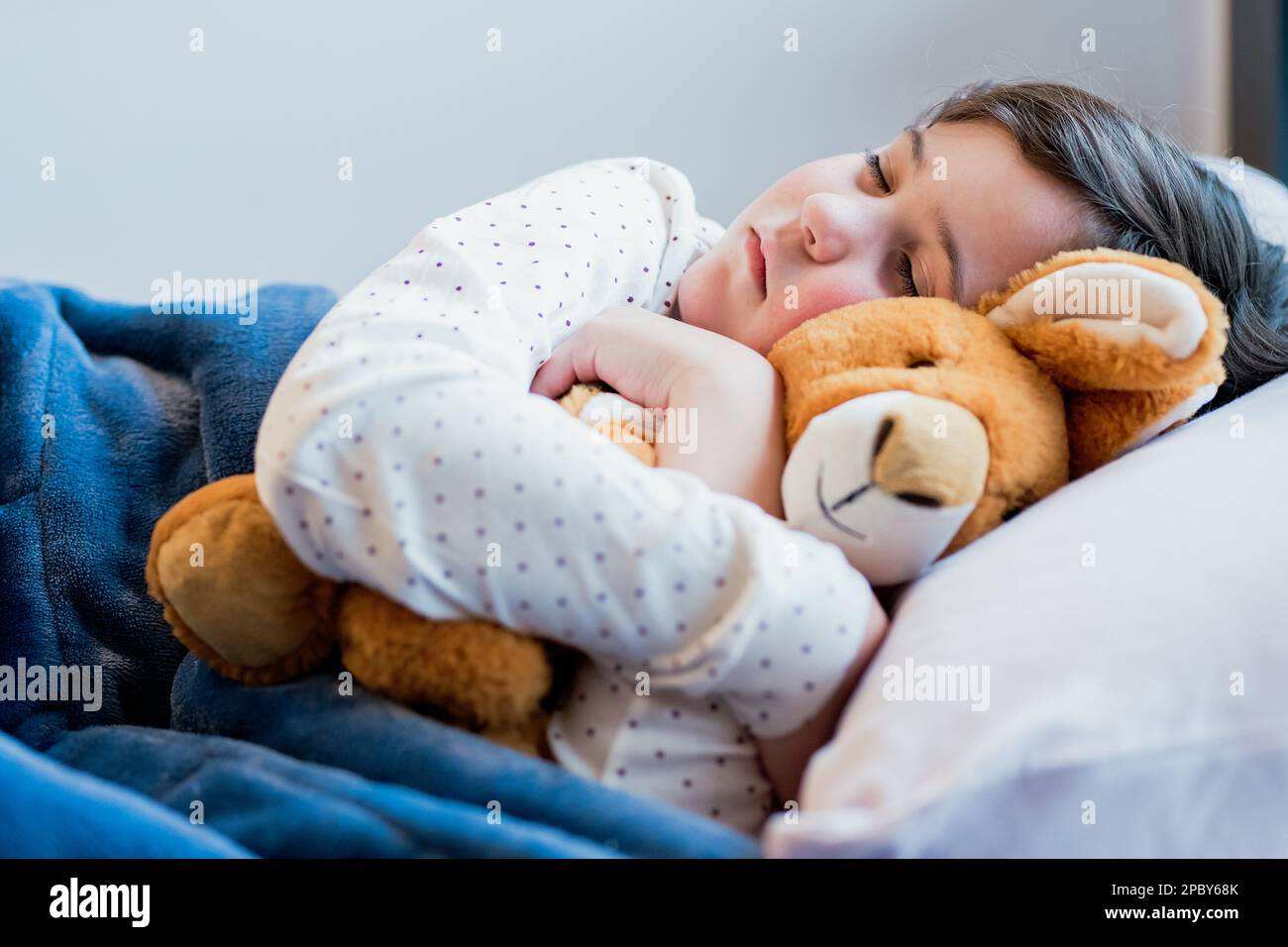 Jolie petite fille en pyjama dormant sur un oreiller blanc doux et enveloppant un jouet doux Banque D'Images
