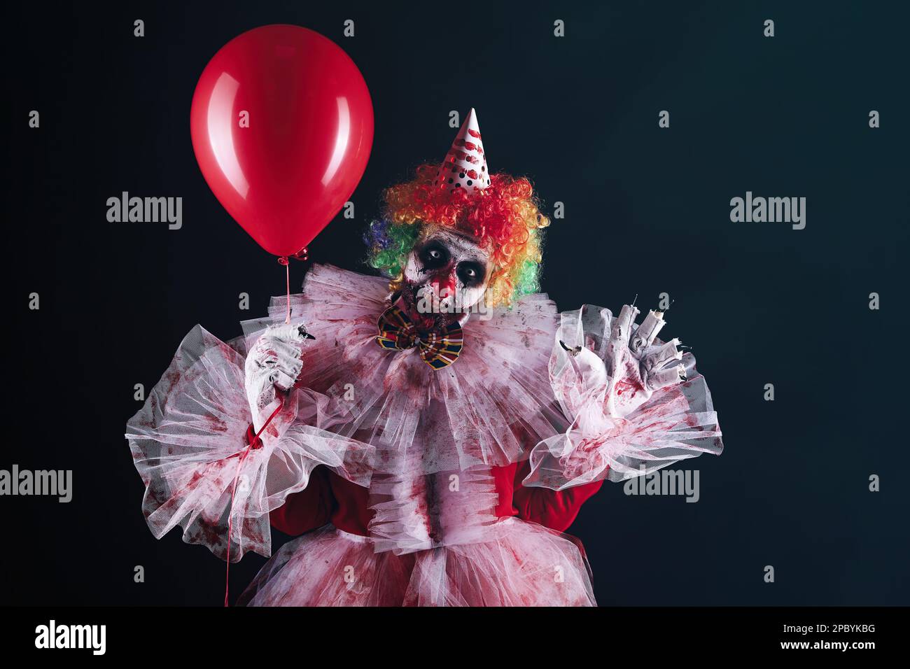 Clown terrifiant avec ballon d'air rouge sur fond noir. Costume de fête d'Halloween Banque D'Images
